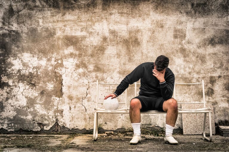Male athlete sitting alone on bench, head in hand, representing the emotional and cognitive challenges of daily life with CTE.