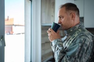 A soldier in military uniform drinks coffee while looking pensively out a window, representing the quiet strength of veterans seeking PTSD treatment in Virginia