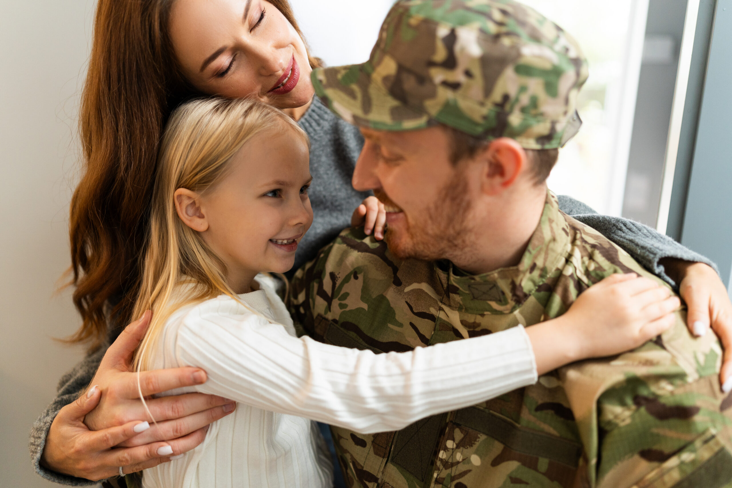A military father in uniform embraces his wife and young daughter at home, sharing a warm and hopeful family moment after seeing a psychiatrist